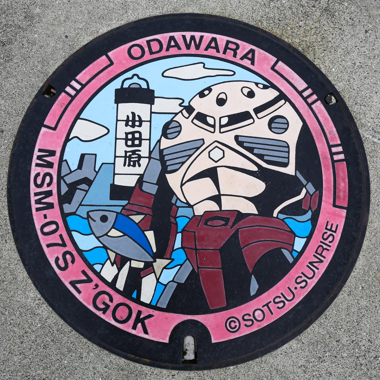 シャア専用ズゴックのガンダムマンホール。小田原漁港にあるちょうちん灯台を背景に、シャア専用ズゴックと小田原市を代表する春の魚であるアジをデザイン