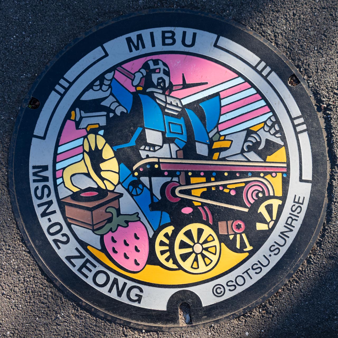 MSN-02 ジオングのガンダムマンホール。蒸気自動車(ペンデルプリンセス号)と蓄音機(エジソンコレクション)、壬生町の名産のいちごを施したデザイン